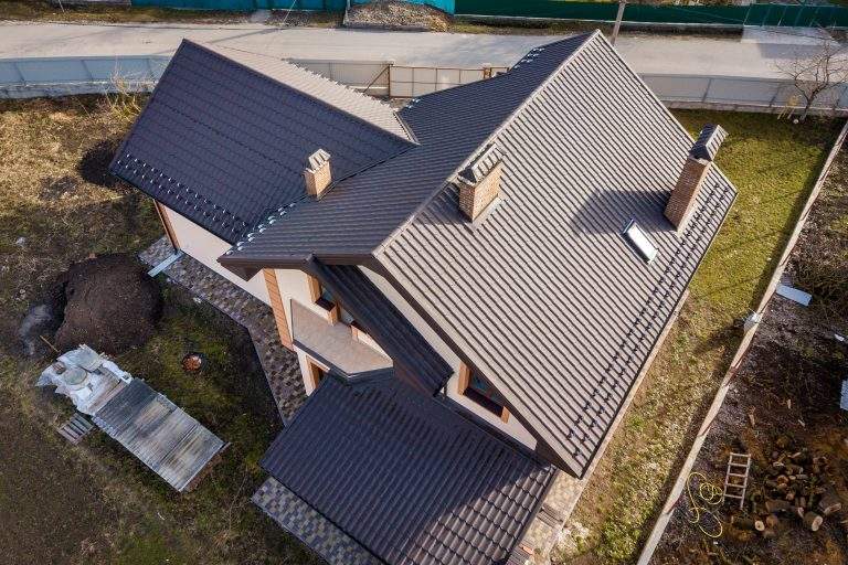 Aerial top view of building steep shingle roof, brick chimneys and small attic window on house top with metal tile roof. Roofing, repair and renovation work.