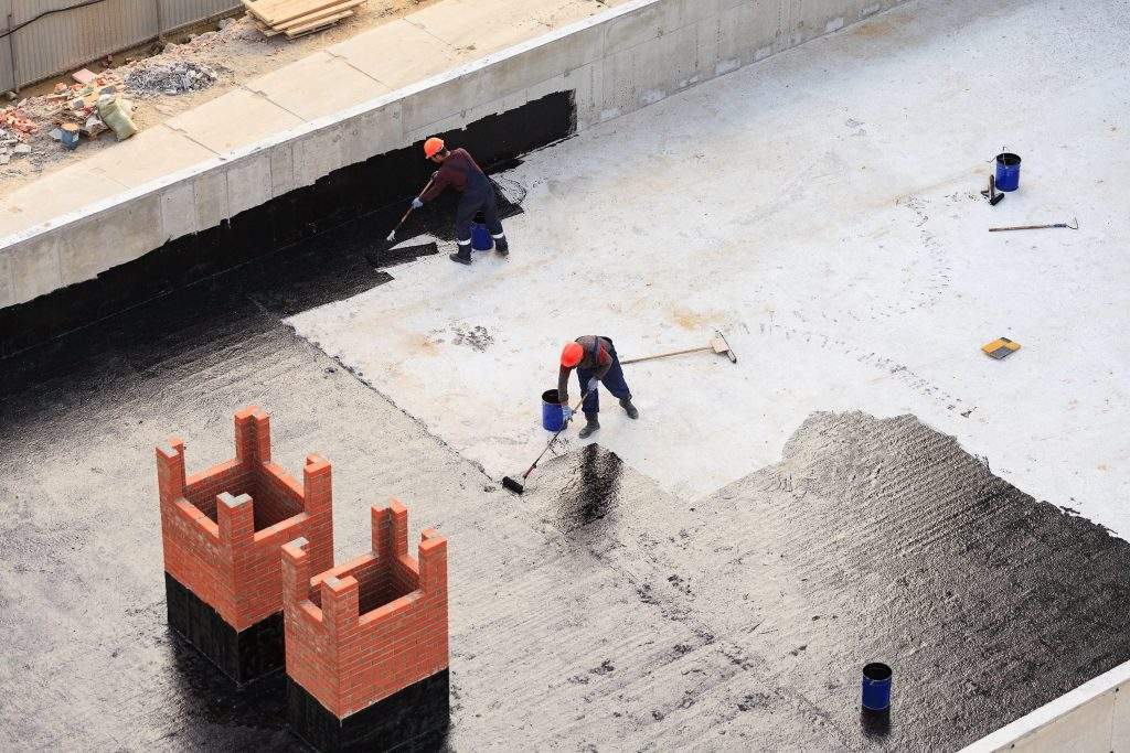 Two workers conduct waterproofing of the roof with bitumen. View from above.