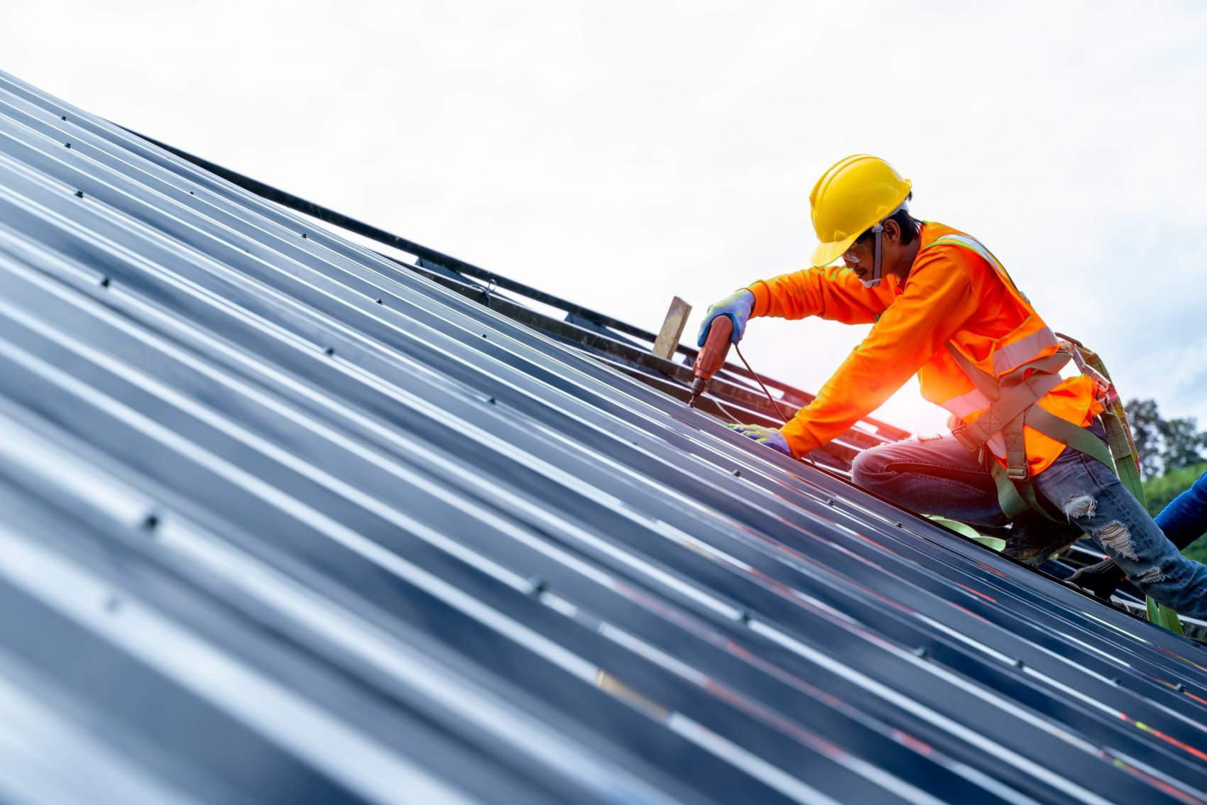 Roofer worker in protective uniform wear and gloves, using air or pneumatic nail gun and installing asphalt shingle on top of the new roof,Concept of residential building under construction.