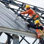 2 workers for construction, installing metal roofing tools, sheet metal New electric drill tool used on a new roof with metal sheets.